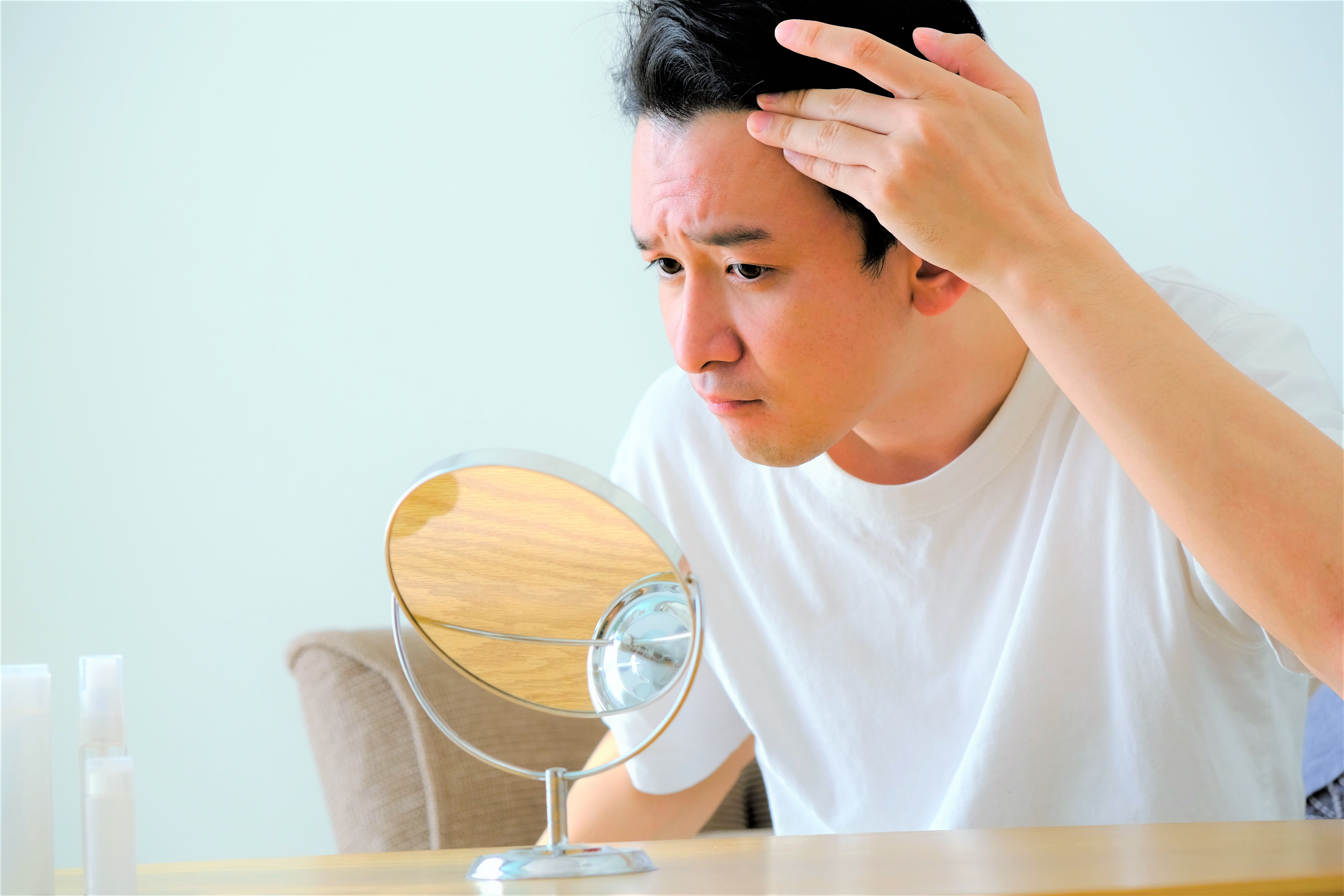 鏡を見ながら生え際の状態を確認する男性