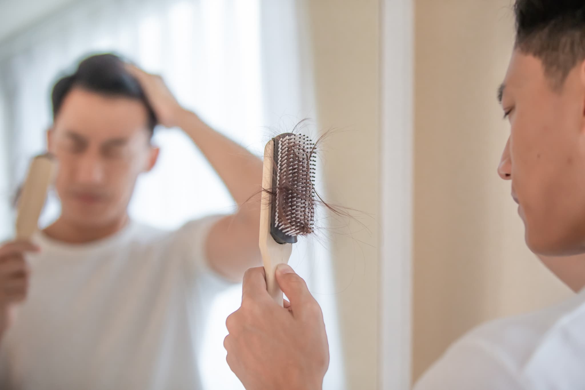 ヘアブラシに絡まった抜け毛を見ている男性